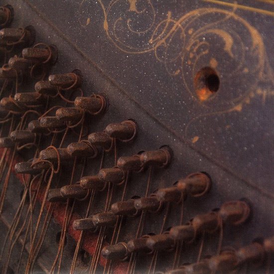 Gros plan des cordes d'un piano avec des chevilles d'accordage rouillées et des motifs décoratifs dorés sur fond sombre.