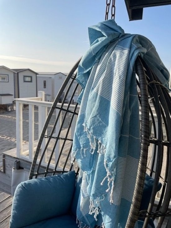 Turquoise hamamdoek met witte strepen en franjes, hangend over een schommelstoel buiten.
