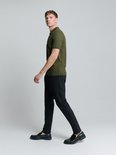 Man draagt legergroen gebreid poloshirt met korte mouwen en zwarte broek, van opzij gezien.