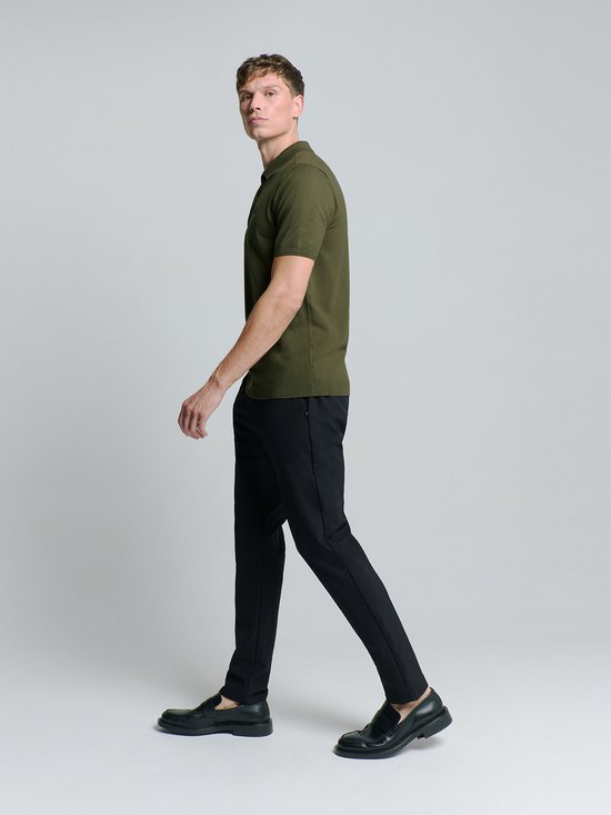 Man draagt legergroen gebreid poloshirt met korte mouwen en zwarte broek, van opzij gezien.