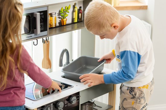 Kinderen spelen met een speelkeuken. Jongen houdt grijze bak vast, meisje bedient kookplaat.
