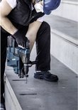 Man met blauwe helm, veiligheidsmasker en handschoenen boort met boormachine