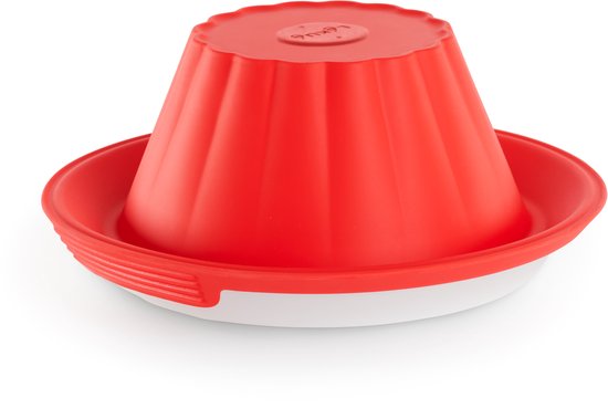 Omgekeerde rode siliconen puddingvorm met geribbelde structuur op een wit keramisch bord.