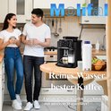 Man en vrouw staan in een keuken met een koffiezetapparaat. Een wit waterfilter staat op de tafel.