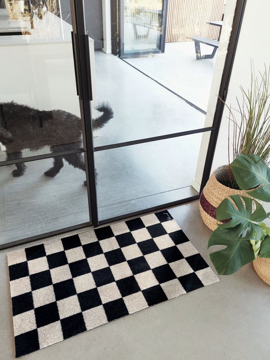 Zwarte en beige geblokte deurmat in een moderne hal, met een hond op de achtergrond.