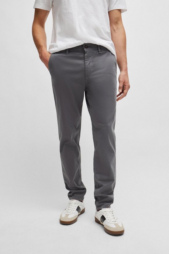 Een man draagt een antracietkleurige chino met een witte t-shirt en beige sneakers. De chino heeft een rechte pasvorm.