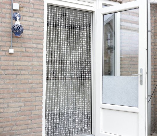 Zwart kralengordijn hangt voor een openstaande witte deur, tegen een bakstenen muur.