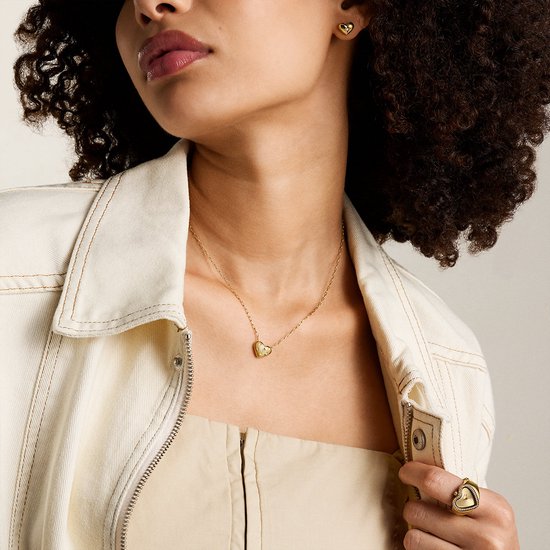 Model draagt een gouden ketting met hartvormige bedel met sterren, bijpassende oorbellen en ring.