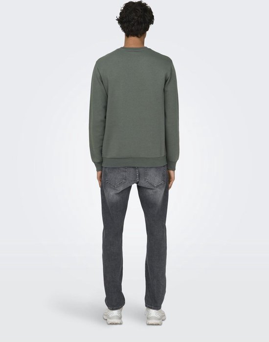 Achterkant van man die naar de camera kijkt. Draagt effen groene sweater en grijze jeans.
