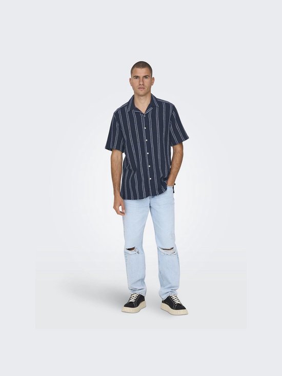 Man in donkerblauw gestreept overhemd en lichtblauwe jeans met scheuren.