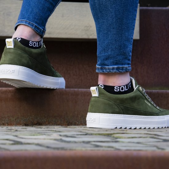 Groene sneakers met witte zolen, gedragen met zwarte SOLIT enkelsokken. Iemand stapt op een trap.