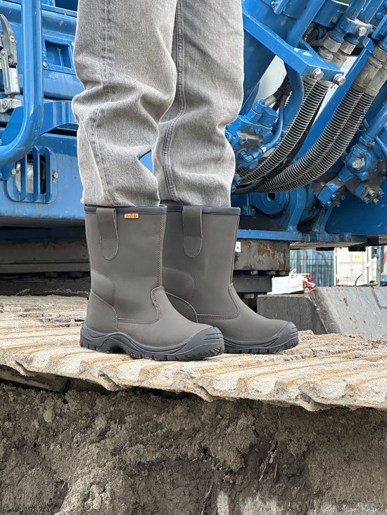 Donkergrijze leren werkschoenen met oranje logo op de zijkant, gedragen met grijze jeans.