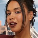 Model met donker haar en opgestoken kapsel, draagt donkerbruine lippenstift en meerdere oorbellen.