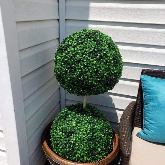 Een tweekoppige buxusboom in een bruine pot, geplaatst naast een bruine stoel met een blauw kussen.