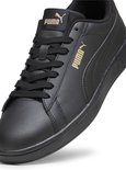 Close-up van de zijkant van een zwarte Puma Smash sneaker met gouden logo.