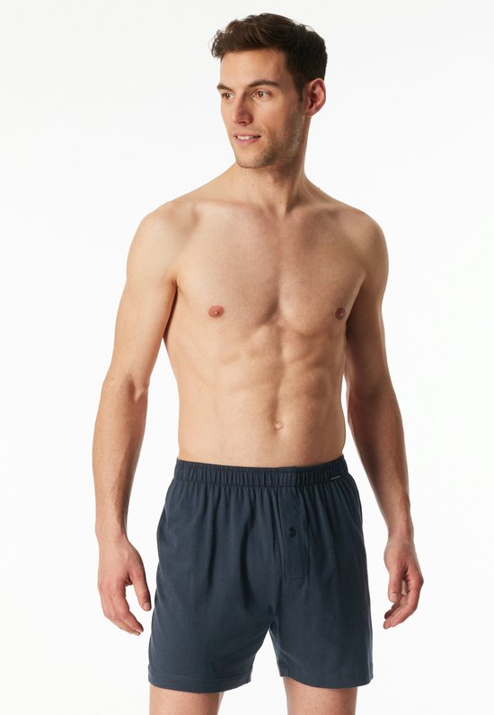 Model met donkerblauwe boxesshorts met knoopsluiting, staand, kijkend naar de zijkant.
