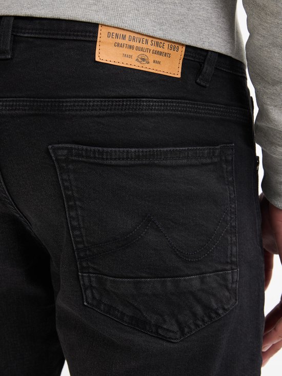 Detail van een zwarte jeans met twee achterzakken, het rechter zakje met sierstiksels.