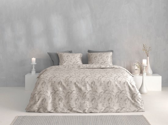 Een tweepersoonsbed opgemaakt met een lichtbeige dekbedovertrek met een grijs gebladerte patroon. Twee grijze kussens liggen achter twee bijpassende kussenslopen.