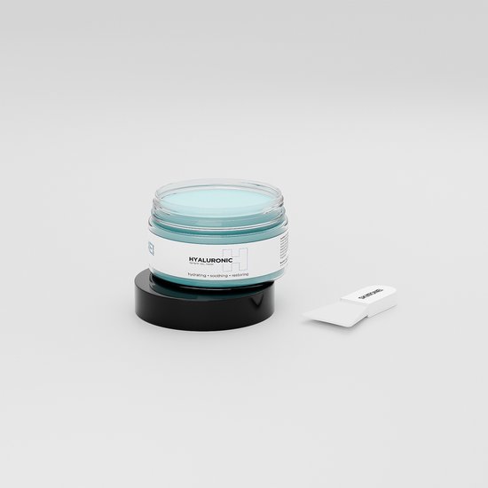 Glazen pot met lichtblauwe gel en zwart deksel, op een platte zwarte schijf met spatel ernaast.