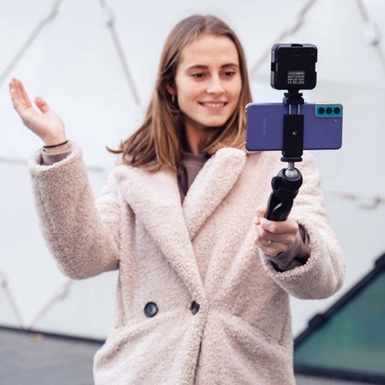 Vrouw met lichte teddy jas houdt een paarse smartphone met een wit LED lampje erop vast.