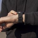Persoon die een zwarte smartwatch met rubberen band aan de pols vastzet.
