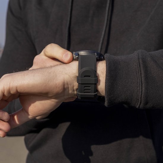 Persoon die een zwarte smartwatch met rubberen band aan de pols vastzet.