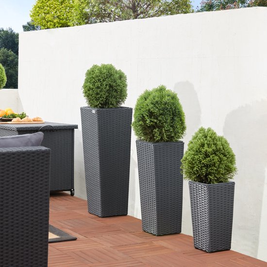 Drie donkergrijze polyrotan bloempotten met gevlochten textuur, gevuld met groene struiken, op een terras.