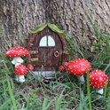 Une petite maison féerique avec des champignons rouges à pois blancs, devant un tronc d'arbre et de l'herbe.