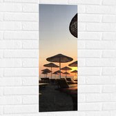 WallClassics - Muursticker - Strand met Ligbedden en Rieten Parasols - 30x90 cm Foto op Muursticker