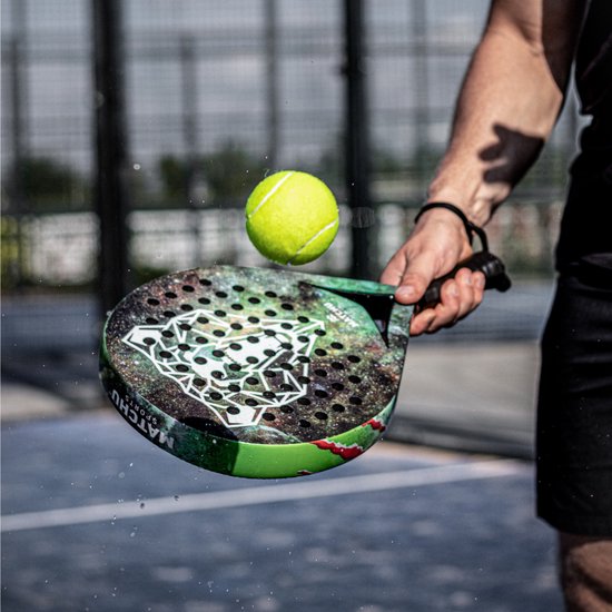 Een man met een zwarte arm band slaat een gele padelbal met een groen, zwart en wit padel racket.