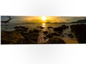 PVC Schuimplaat- Zon verdwijnend achter Wolken boven de Zee vol Rotsen - 90x30 cm Foto op PVC Schuimplaat