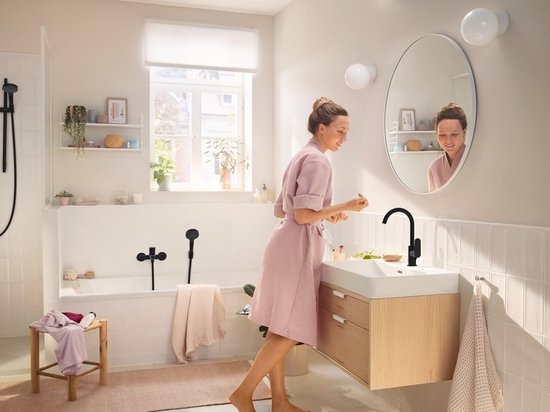 Een vrouw in een badjas bij een wastafel met een matzwarte kraan in een moderne badkamer.