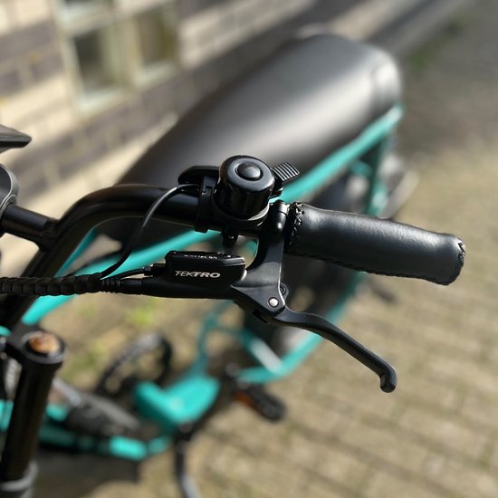 Zwarte fietsbel op het stuur van een turquoise elektrische fiets met een zwart zadel en handvatten.