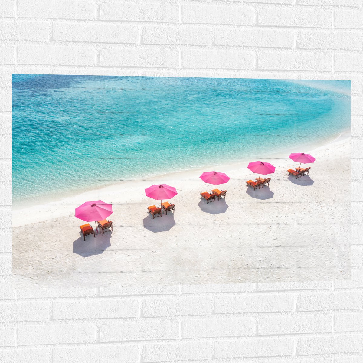 Muursticker - Ligbedden onder Roze Parasols op het Witte Strand bij Blauwe Oceaan - 105x70