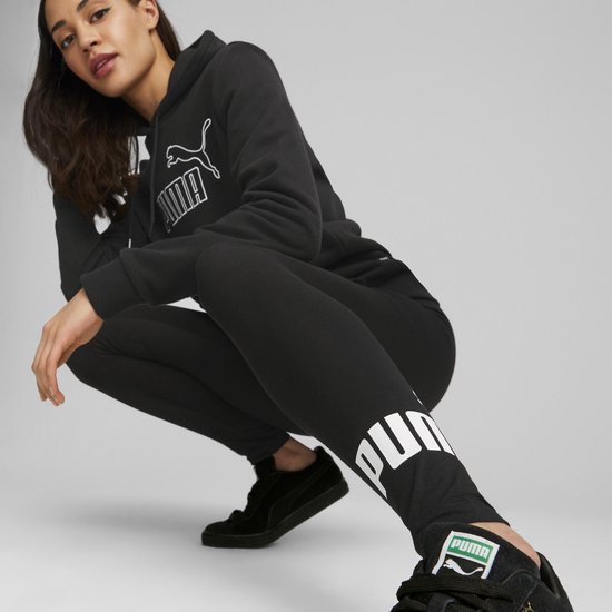 Vrouw in zwart Puma outfit, hoodie en legging met Puma-logo, zittend op de grond.