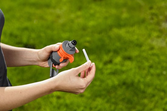 Handen die de GARDENA turbinesproeier vasthouden en een witte pin bevestigen