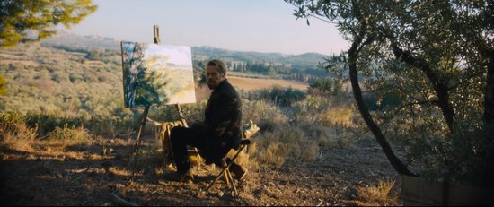 Willem Dafoe schildert een landschap in de buitenlucht, zittend op een klapstoel voor een ezel.