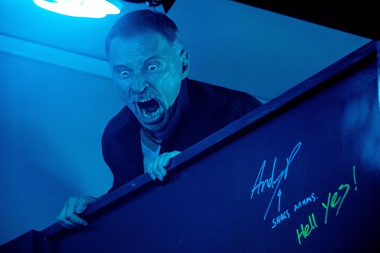 Man met snor en open mond schreeuwt fel verlicht in blauw met graffiti op de muur.