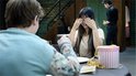 Een vrouw met lange donkere haar verbergt haar ogen terwijl ze glimlacht bij een gift box.