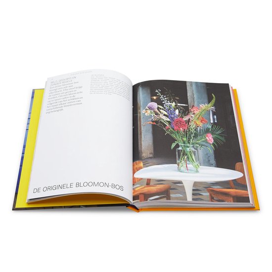 Open boek met tekst en een foto van een kleurrijk bloemstuk in een glazen vaas op een ronde tafel.