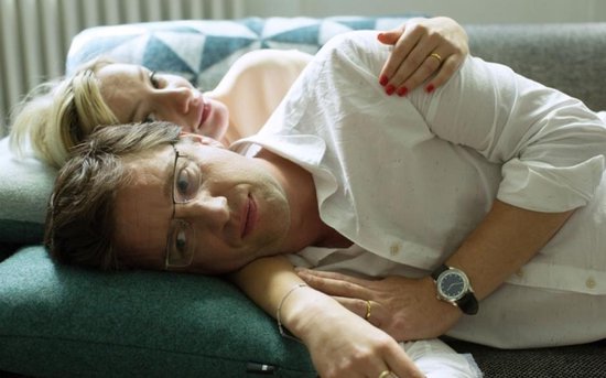Man met bril en witte blouse ligt op schoot van vrouw met blond haar, op een bank.