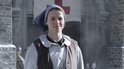 Jonge vrouw in een blauwe hoofddoek en bruin vest lacht, met een rode kruisvlag op de achtergrond.