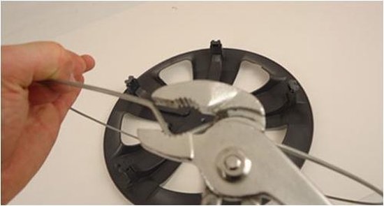 Hand met waterpomptang die een metalen ring om een zwarte wieldop buigt.