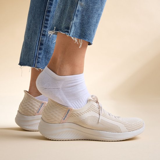 Vrouwen dragen crèmekleurige Skechers sneakers met spijkerbroek.
