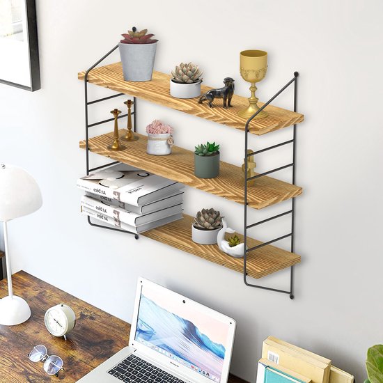 Drie houten planken met decoraties en boeken, boven een bureau met een laptop en wekker.