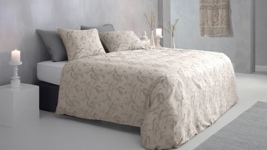 Een tweepersoonsbed opgemaakt met een lichtbeige dekbedovertrek met een grijs gebladerte patroon. Twee grijze kussens liggen achter twee bijpassende kussenslopen.