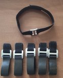 Zwarte bandjes met gespen en een ronde band met gesp, op een houten ondergrond.