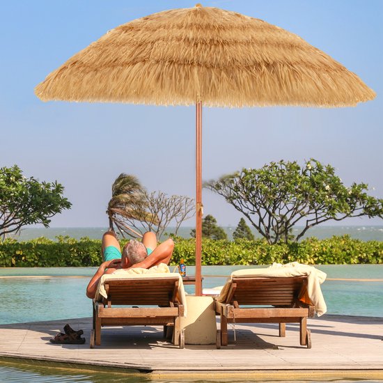 Man ontspant onder een strooien parasol bij een zwembad en de oceaan.