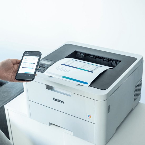 Hand houdt smartphone voor witte Brother printer met document.