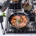 Garnalen sissen in een koekenpan op gasfornuis. Kleine pot met bouillon ernaast.